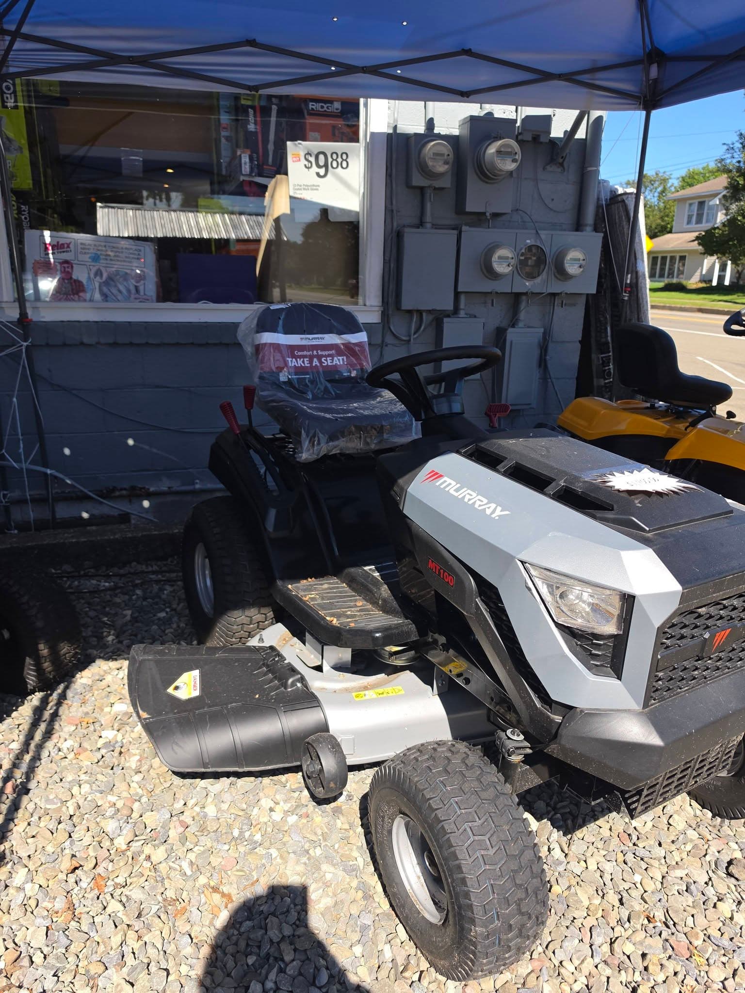Silver and black Murray MT100 riding lawn mower parked on gravel under a blue canopy.