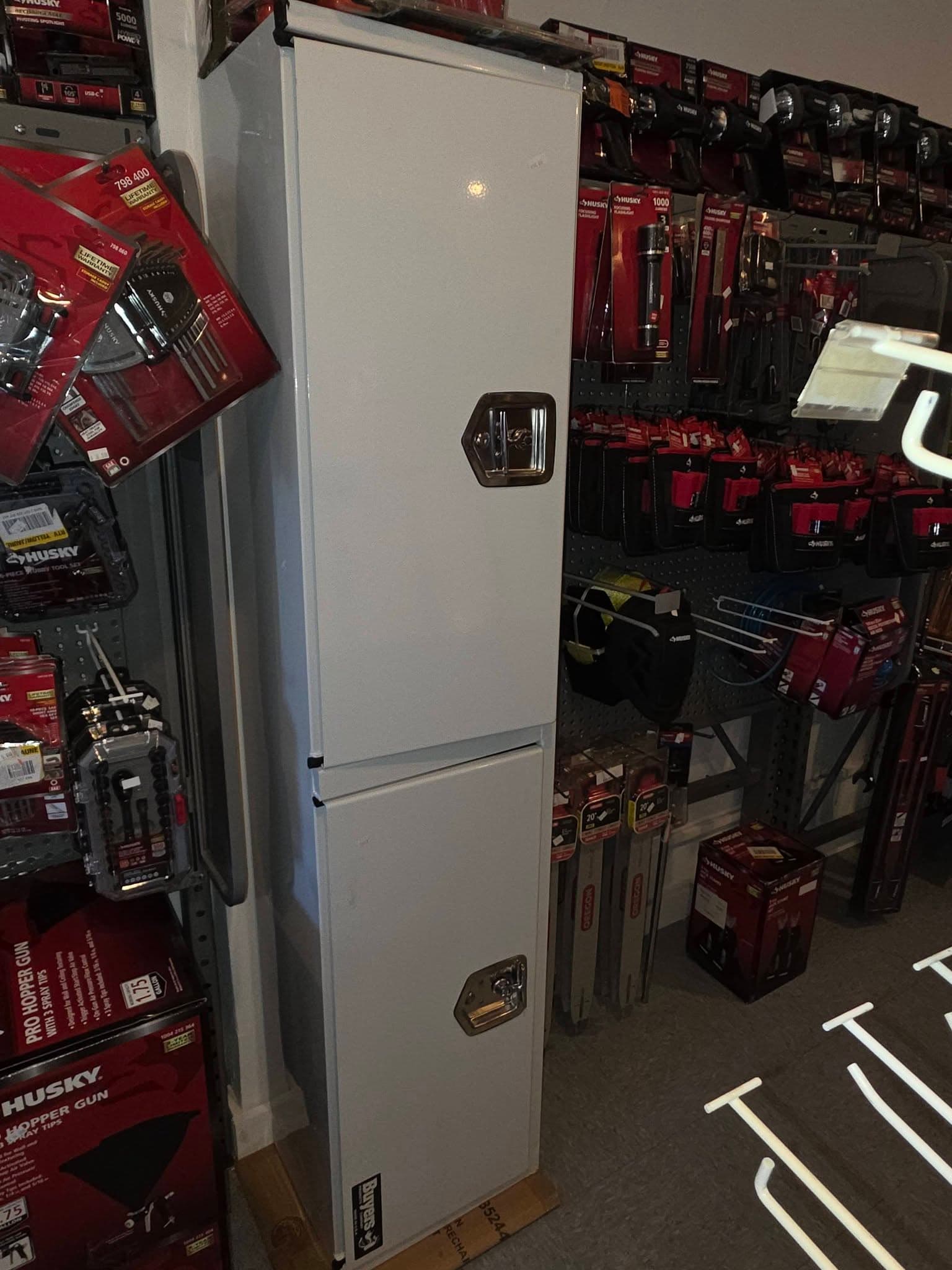 Tall white metal storage cabinet with two doors and silver latches in a tool store.