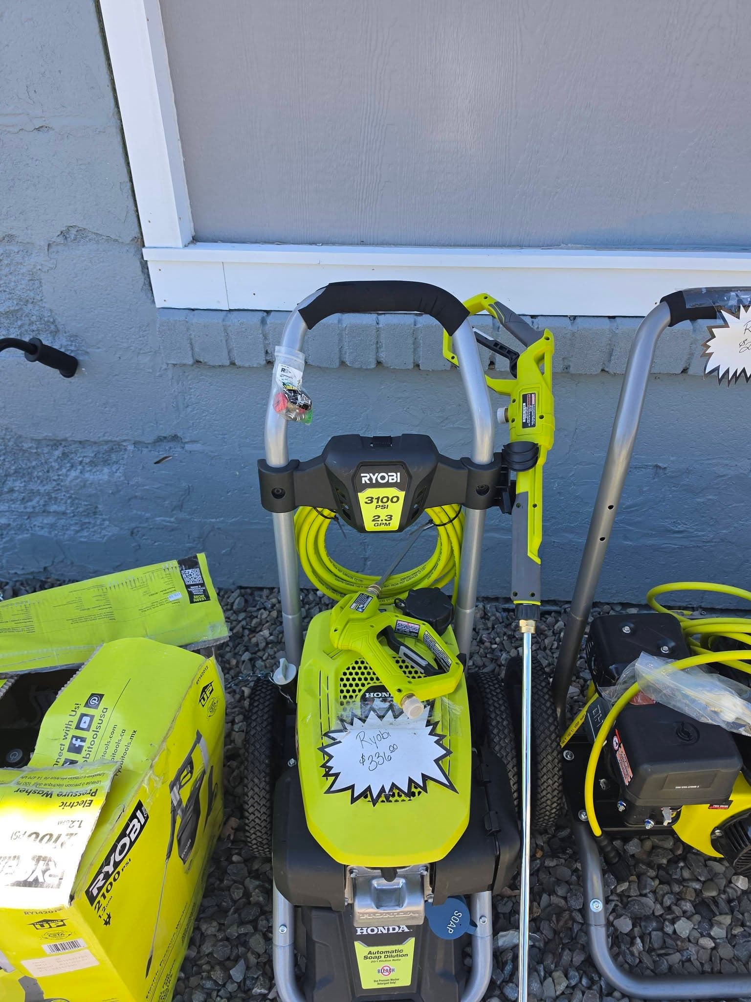 Lime green Ryobi 3100 PSI pressure washer with Honda engine, spray wand, and price tag.
