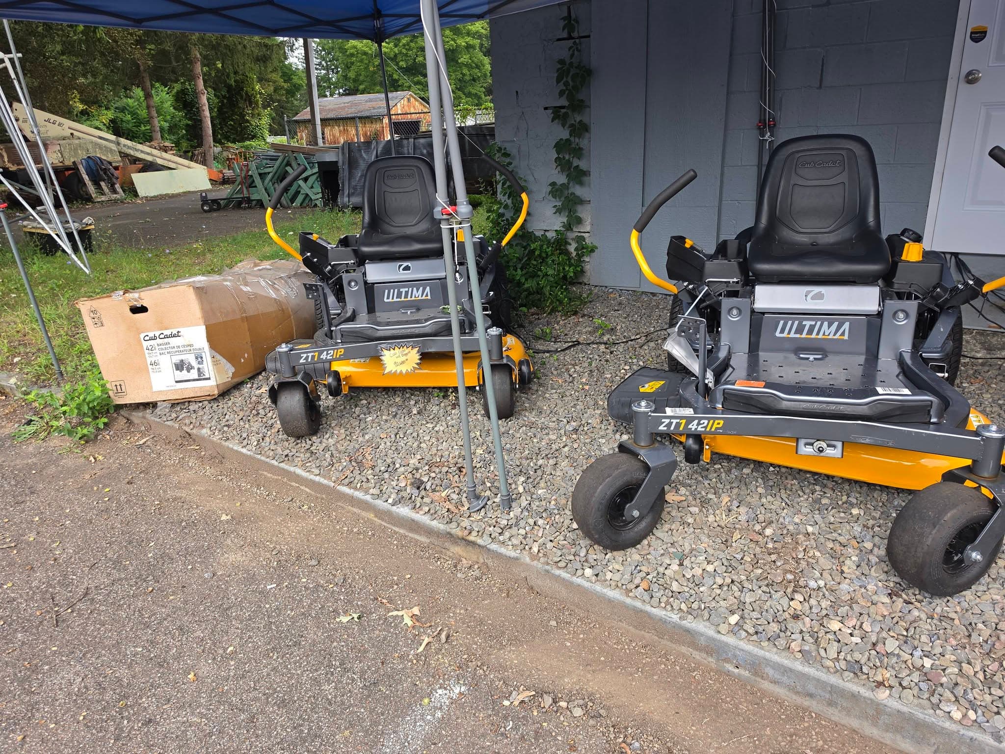 Two Cub Cadet Ultima ZT1 42IP zero-turn mowers parked on gravel under a blue canopy.
