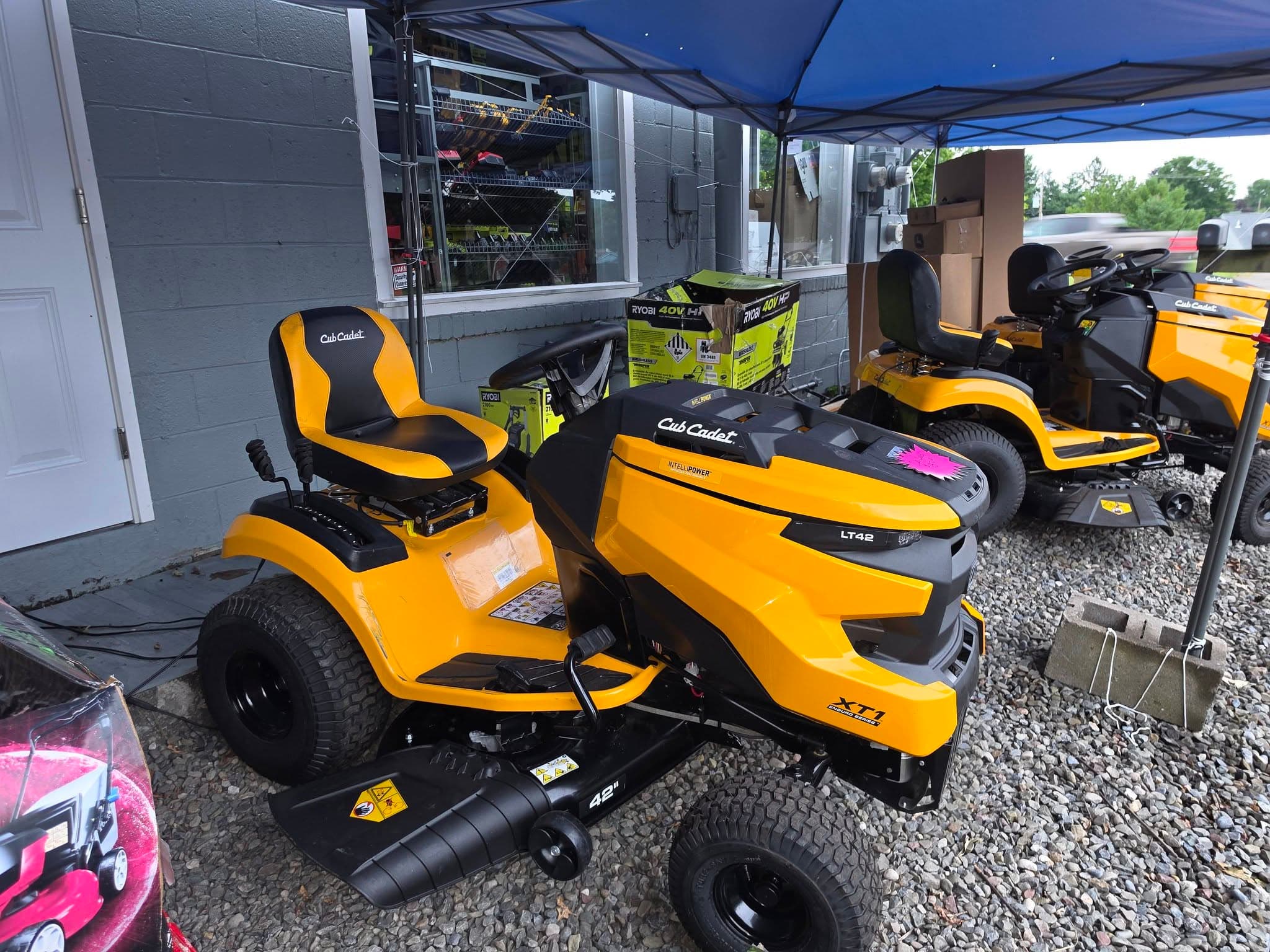Yellow and black Cub Cadet XT1 riding mower parked on gravel under a blue canopy.
