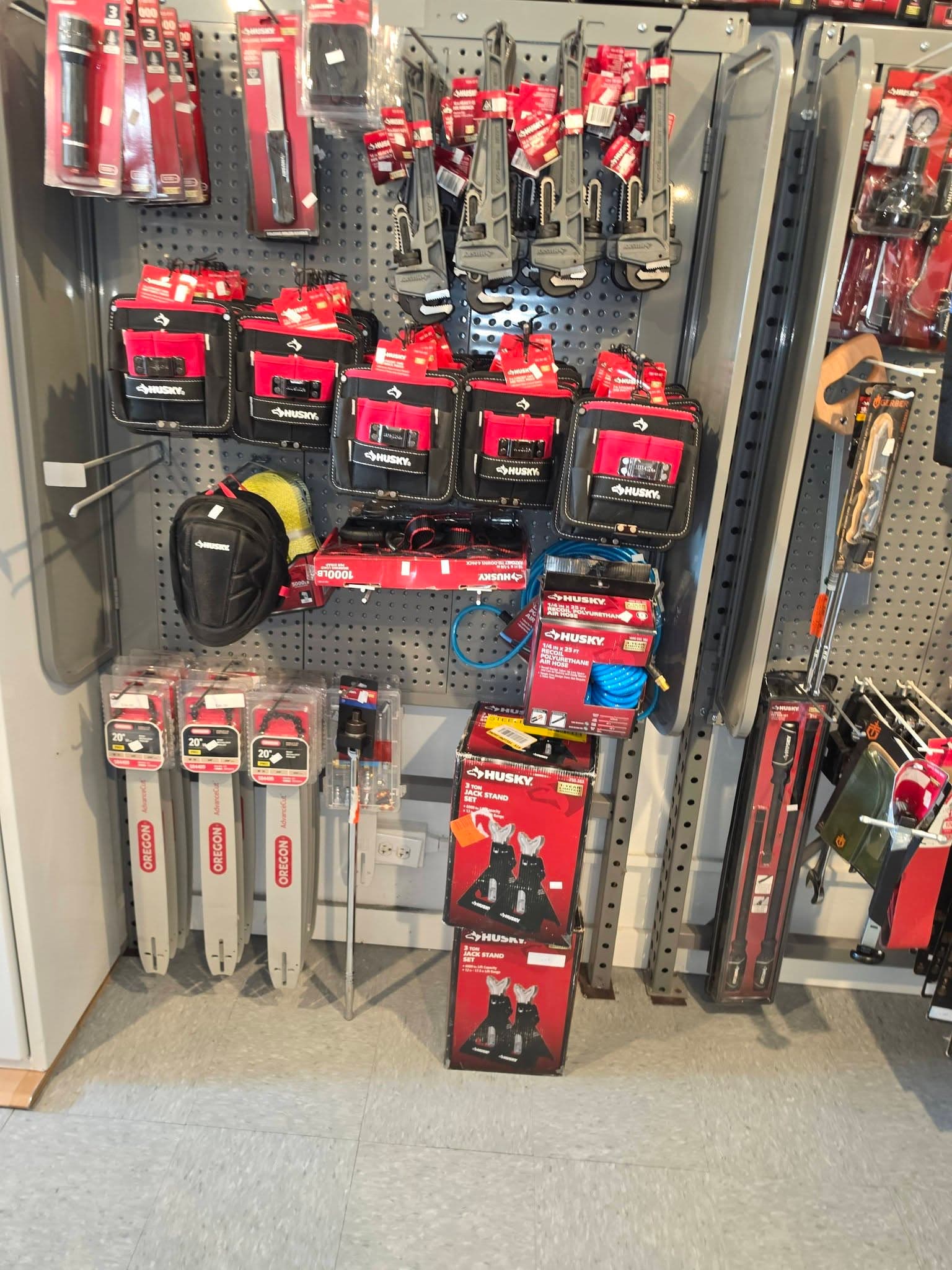 Retail display of Husky tool pouches, jack stands, and Oregon chainsaw bars on a pegboard.